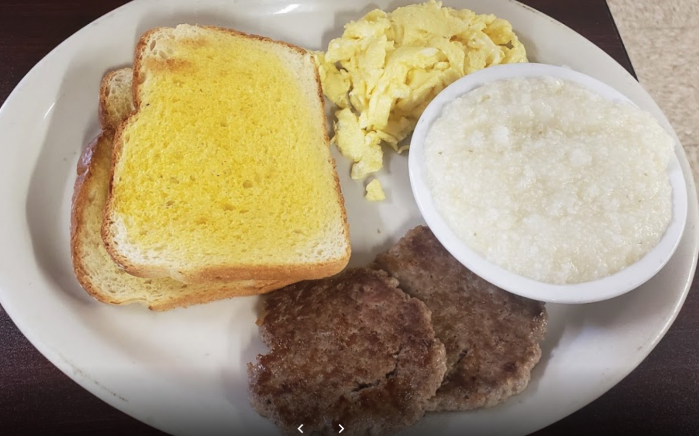 a plated country style breakfast with scrambled eggs, grits, sausage patties and buttered toast