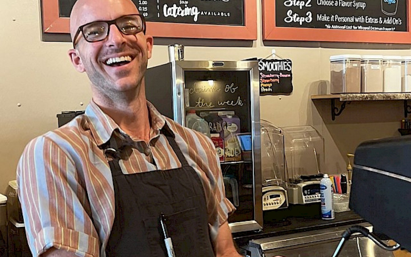 coffee shop employee laughing behind of counter with a customer while preparing his coffee order