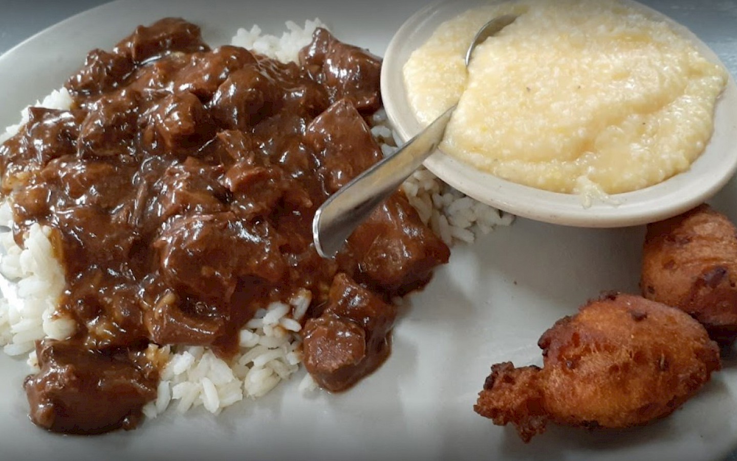 beef tips in gravy on rice, a bowl of cheese grits and hushpuppies