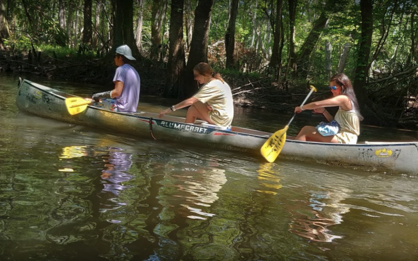 three teenagers paddling along in a canoe