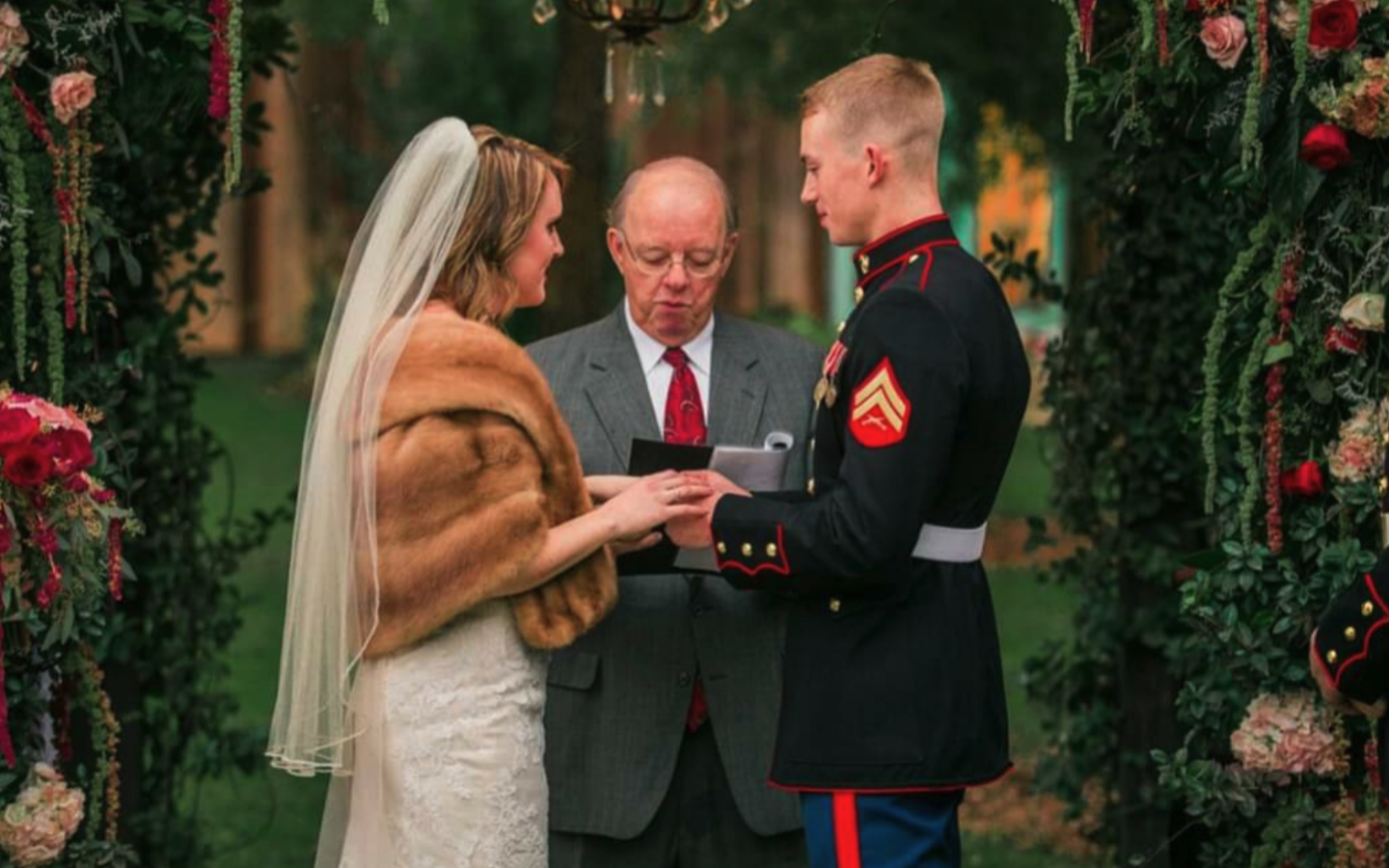 a bride and a male u.s. marine holding hands before a pastor at their wedding