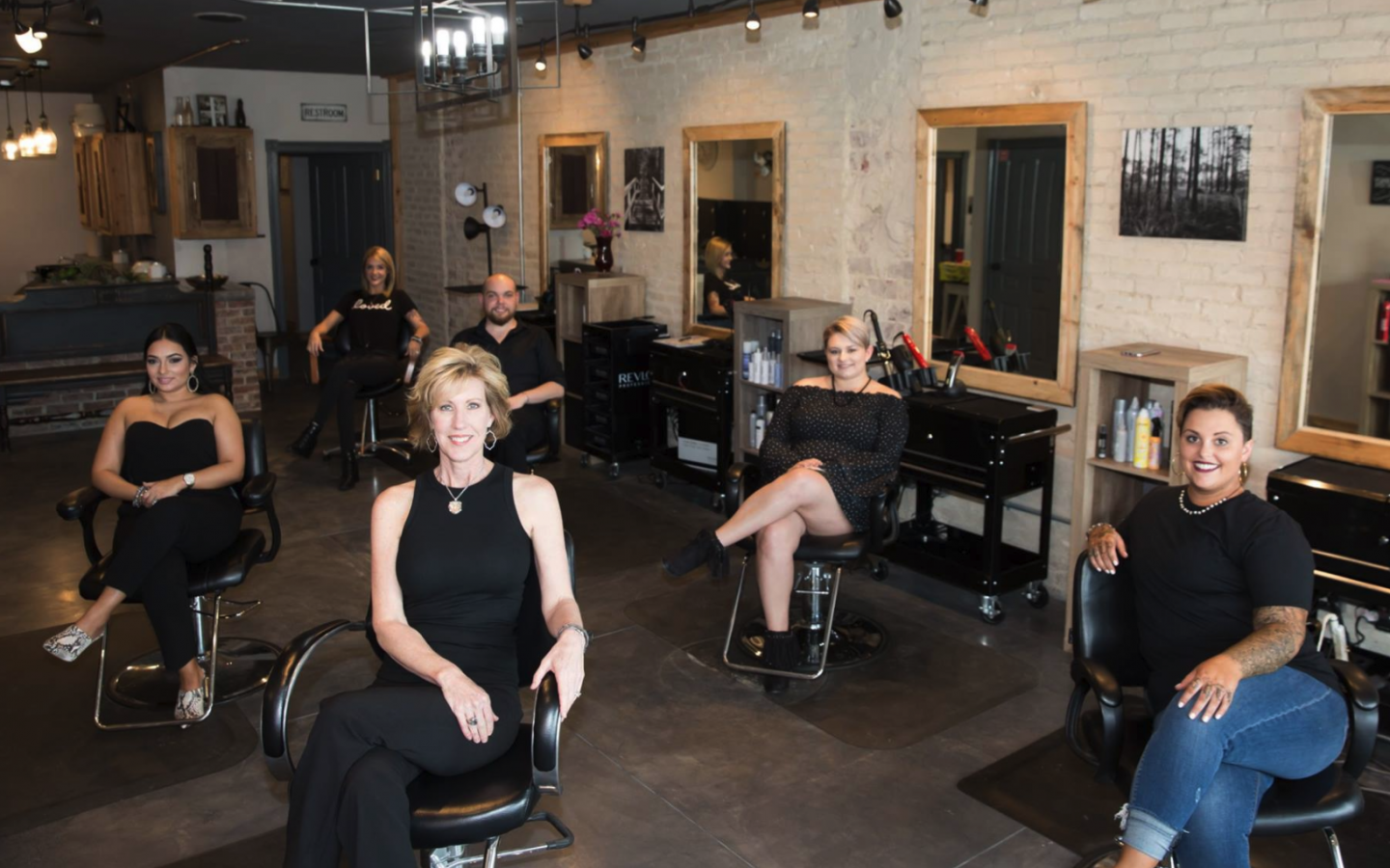 photo of the owner, and five staff members at the styling station sitting in chairs facing the camera