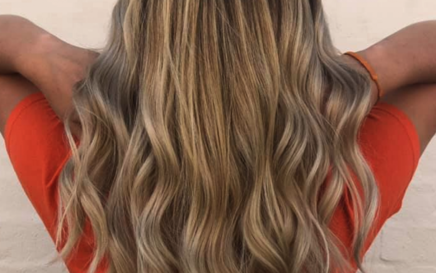 back of a woman's head, with her using her hands to lift up the back of her wavy hair