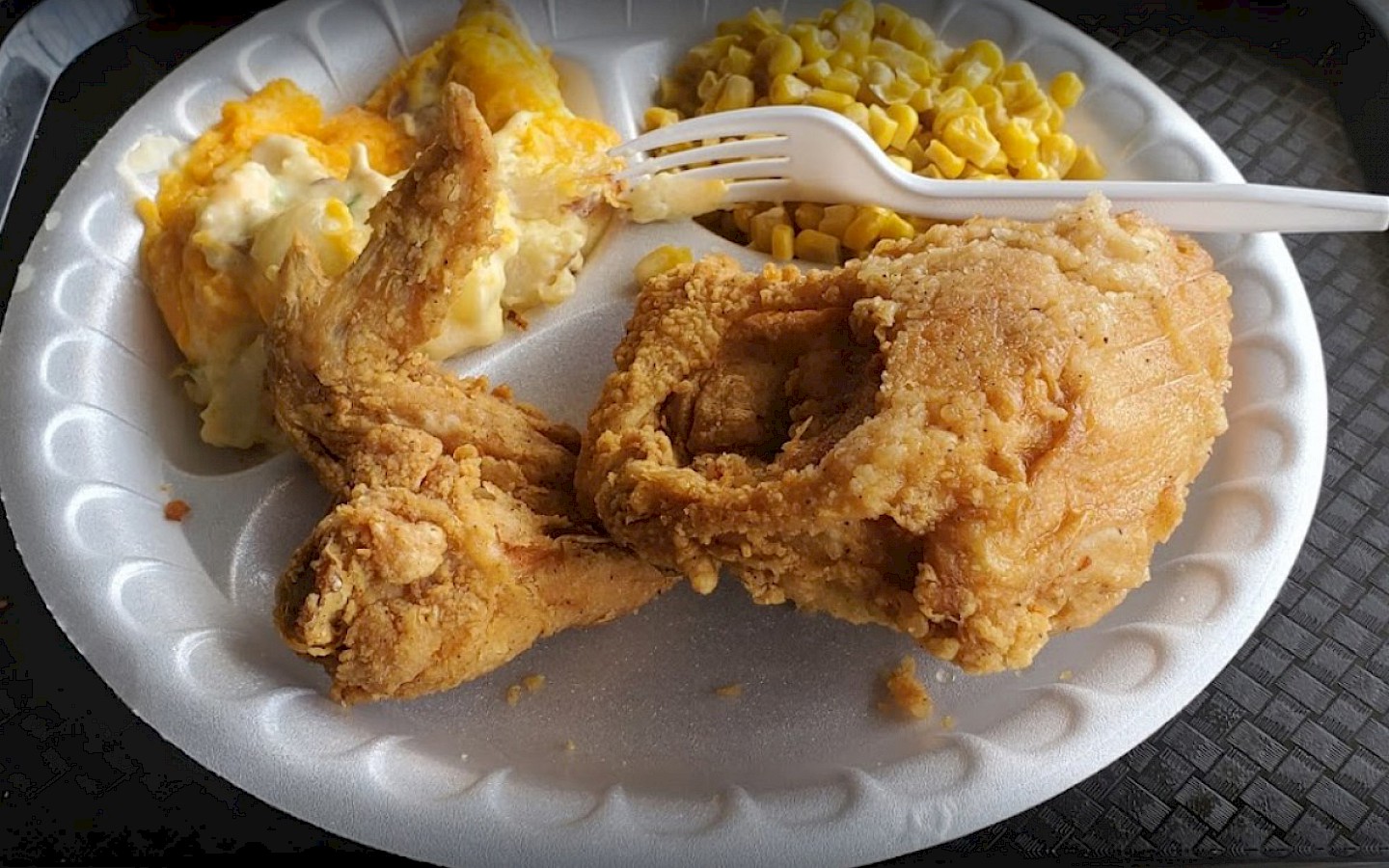 fried chicken along with corn and peach cobbler on a styrofoam plate