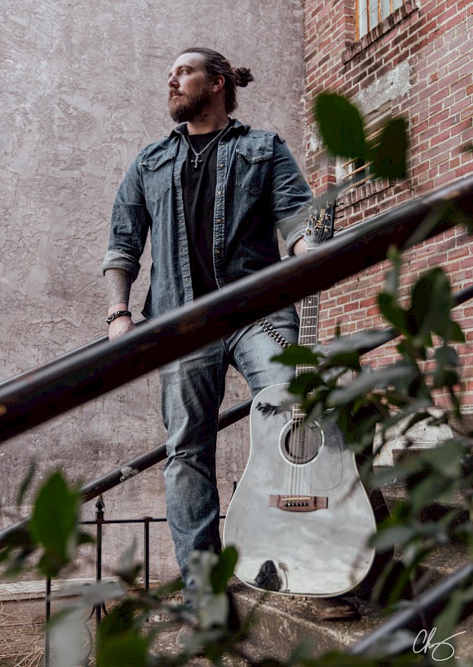 frank fletcher, musician, holding an acoustic guitar while standing on an old metal staircase