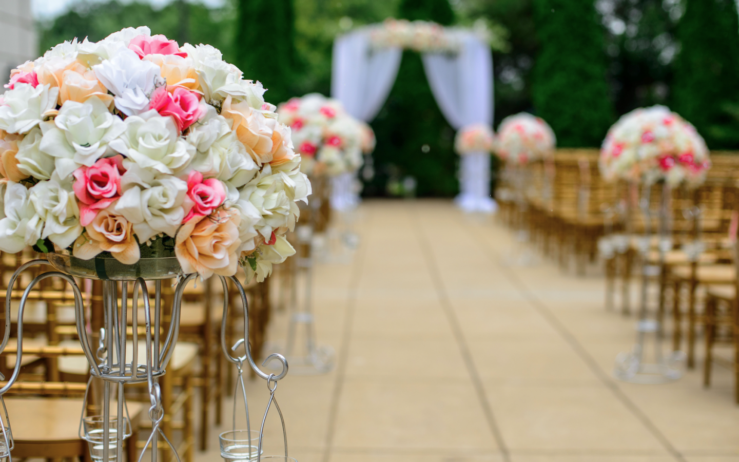 empty wooden chairs next to floral decorations, with a wedding bough in the far background