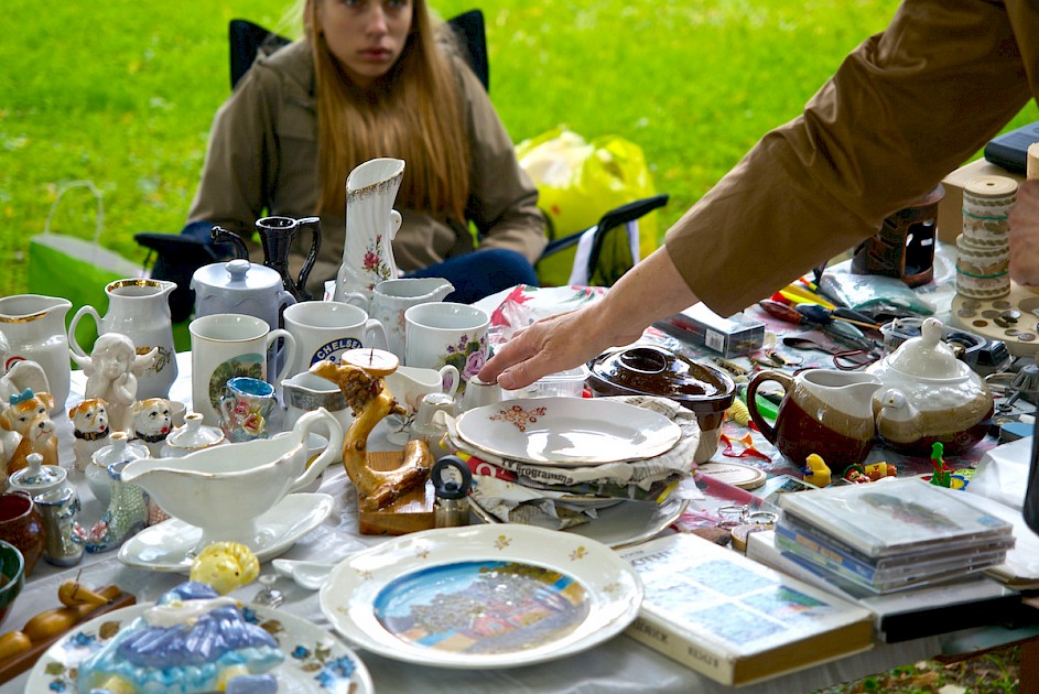 a woman sitting behind a table full of various yard sale items