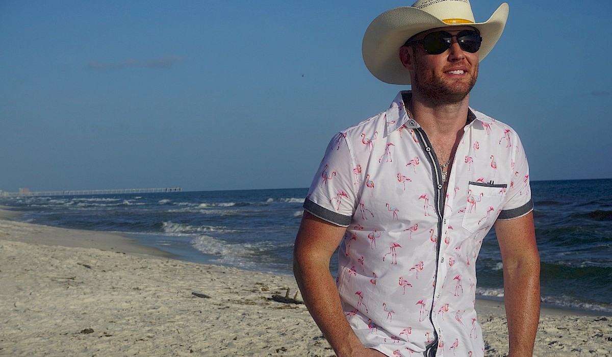 guy with cowboy hat on walking on a sandy beach