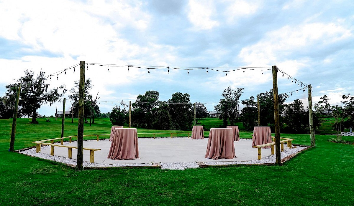 outdoor gathering area with gravel and wooden benches and string lighting at the barn venue