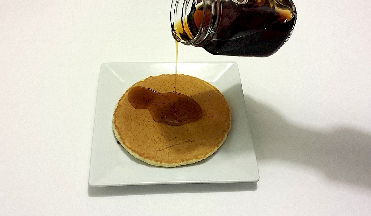 glass jar of syrup pouring onto a pancake on a white plate