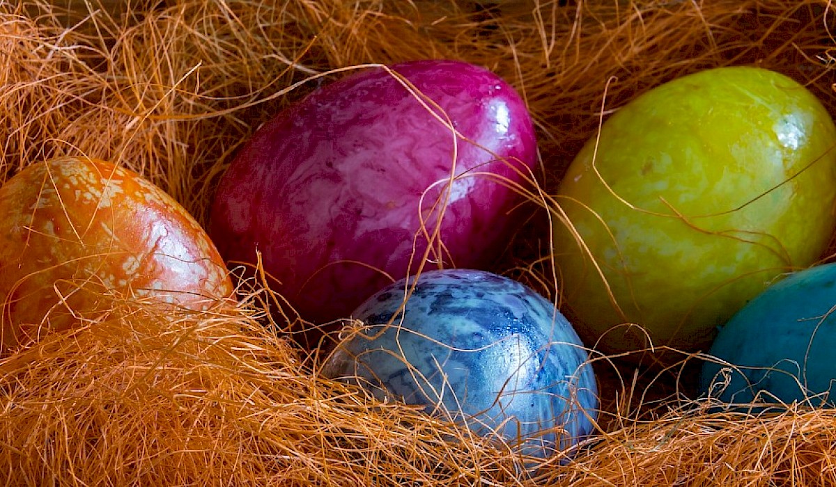 multicolor easter eggs inside an easter basket full of orange grass