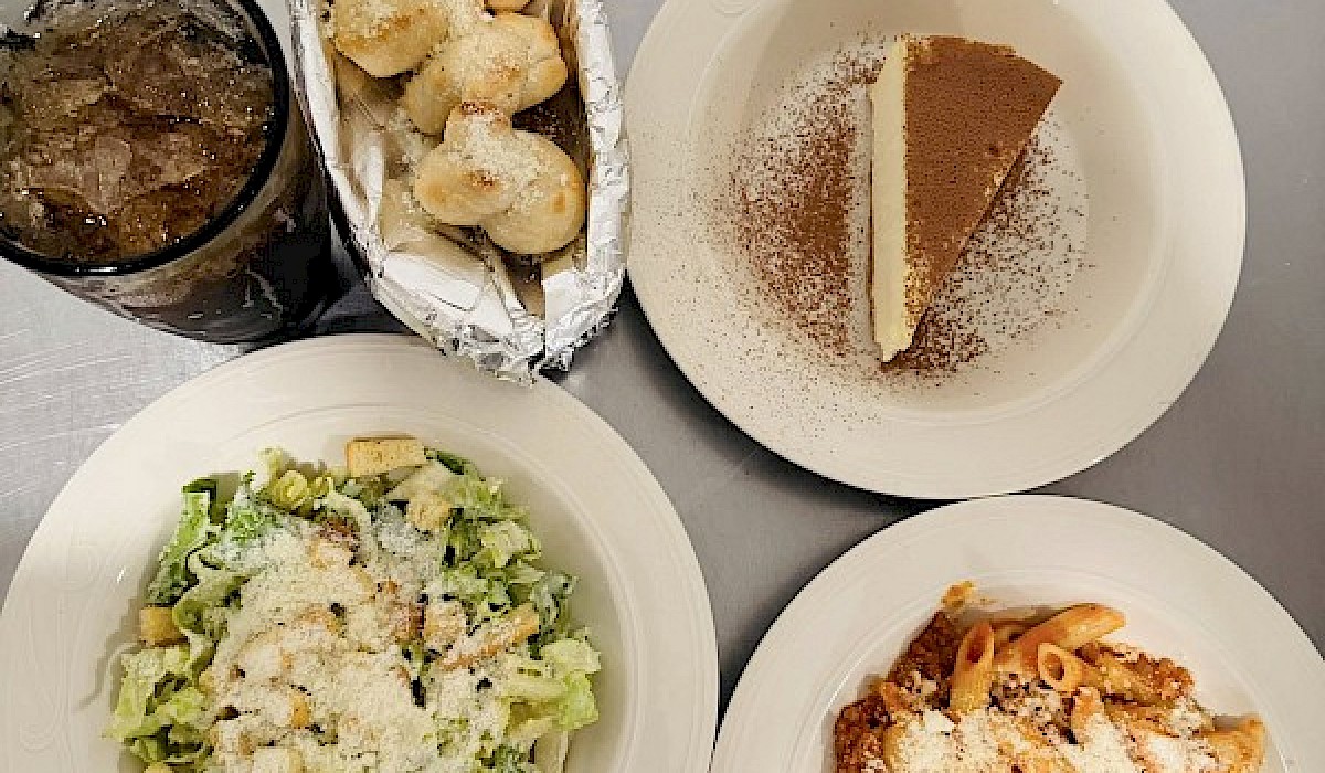 italian meal of pasta, salad, bread and dessert sitting on a restaurant counter