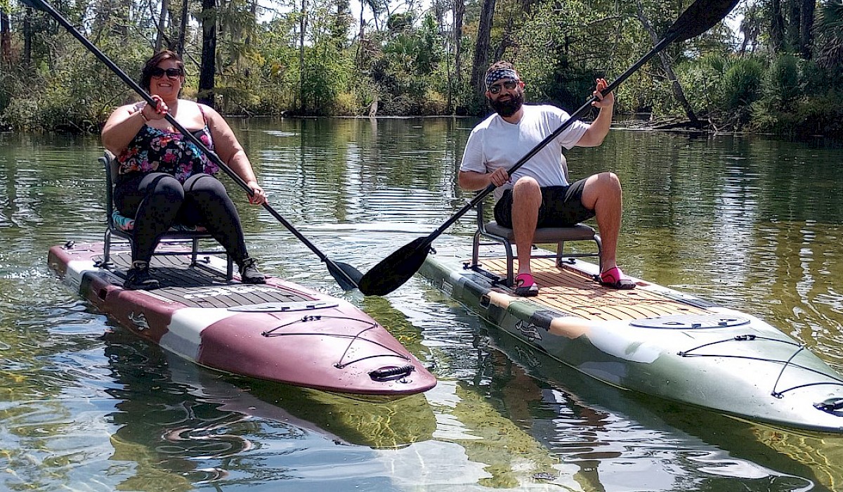 A man and woman sitting on kakus on Econfina Creek holding up their paddles