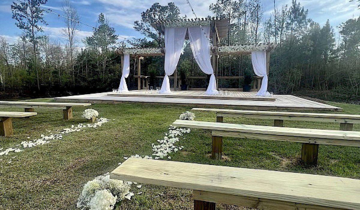 wooden wedding alter draped with white fabric in a field with wooden benches on each side