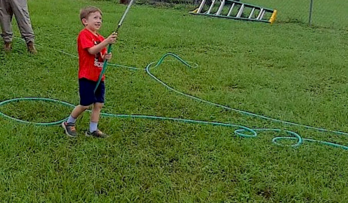 little boy shooting a hose at a bucket suspended on a line above his head during fire games